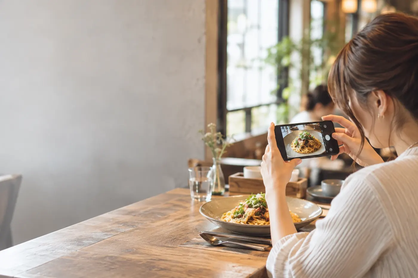 カフェで料理をスマートフォンで撮る女性